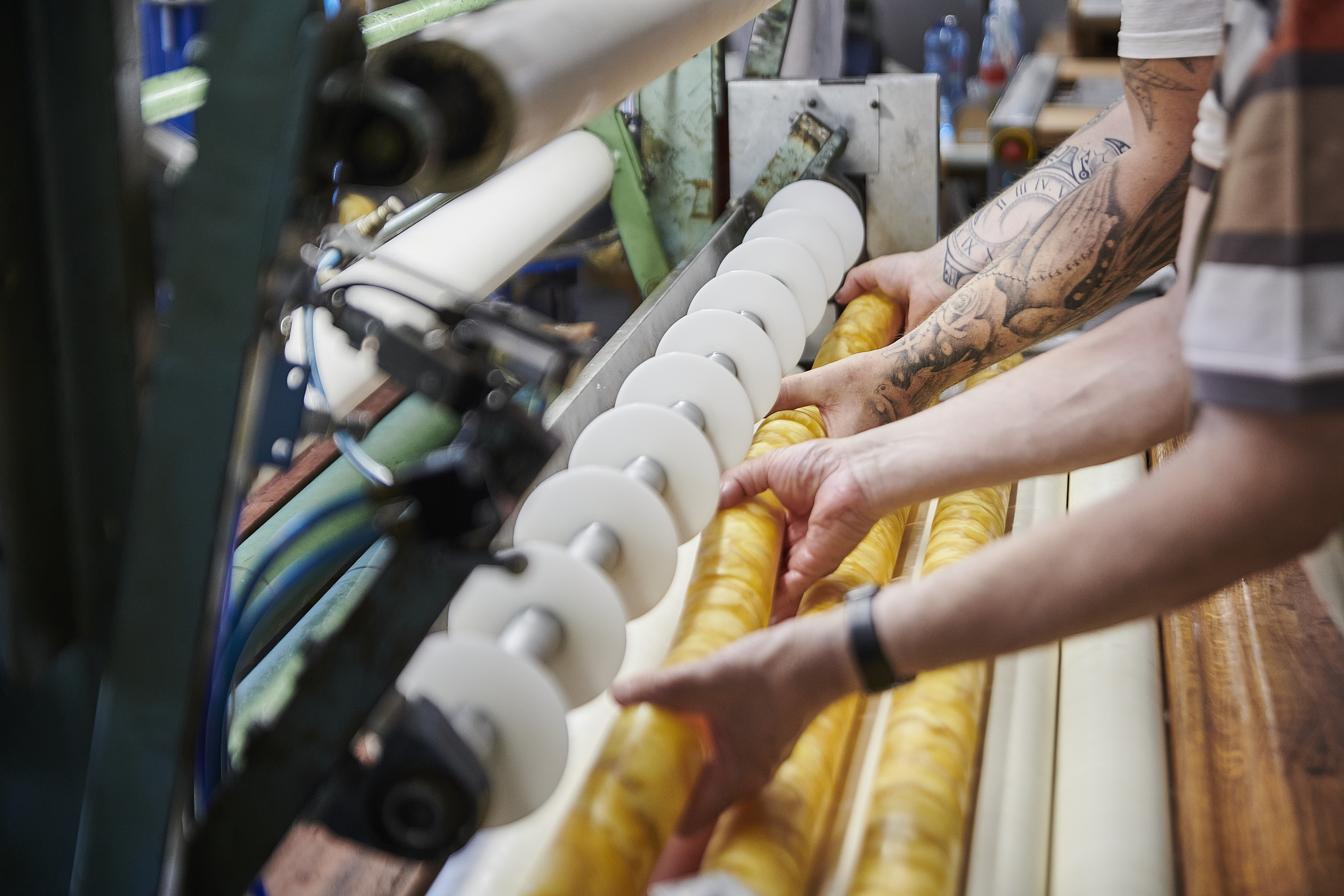 Zwei Paar Hände heben einen Strang Stumpenkerzen aus einer Wachswalze heraus.