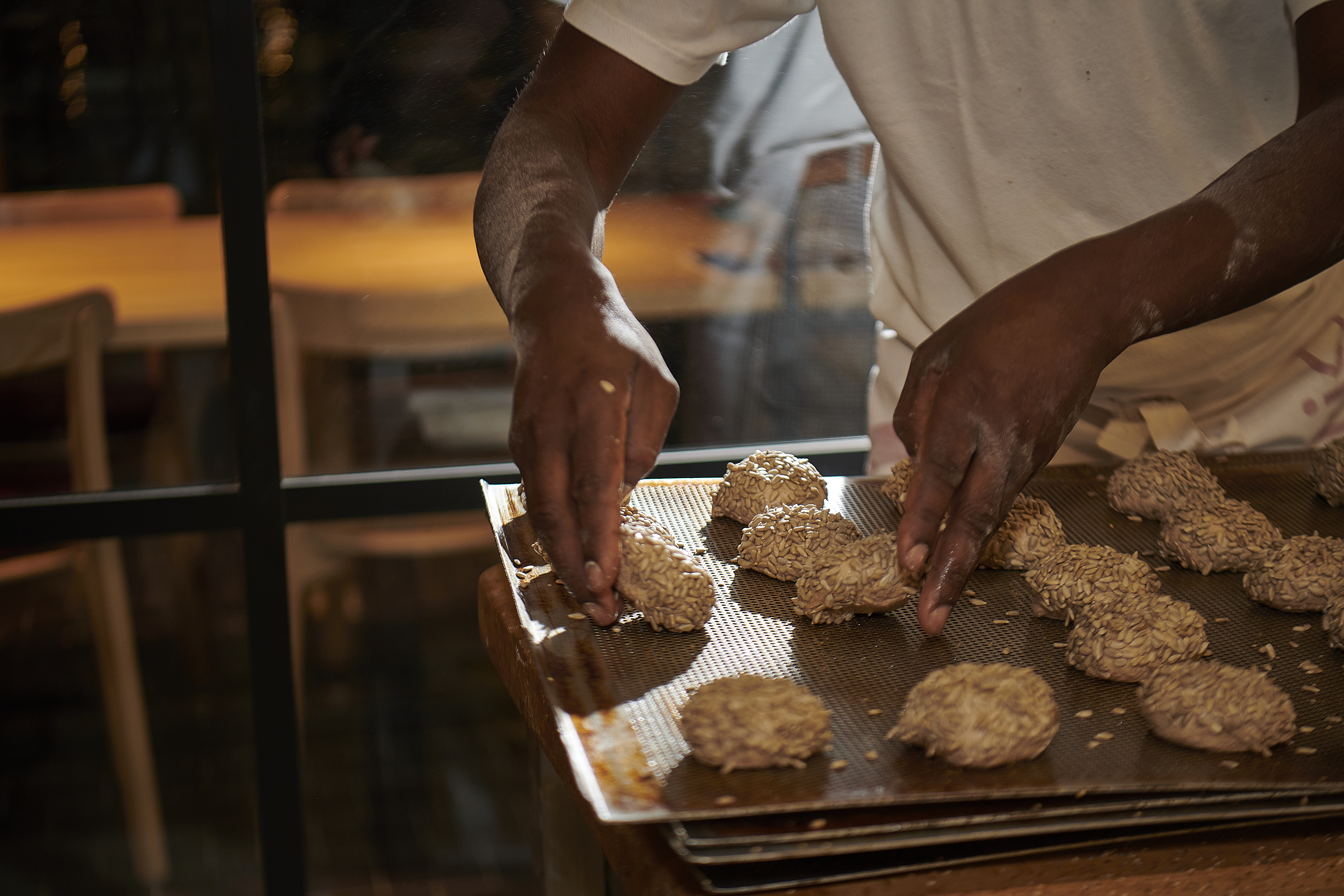 Hände legen Brötchenteiglinge auf ein Backblech.