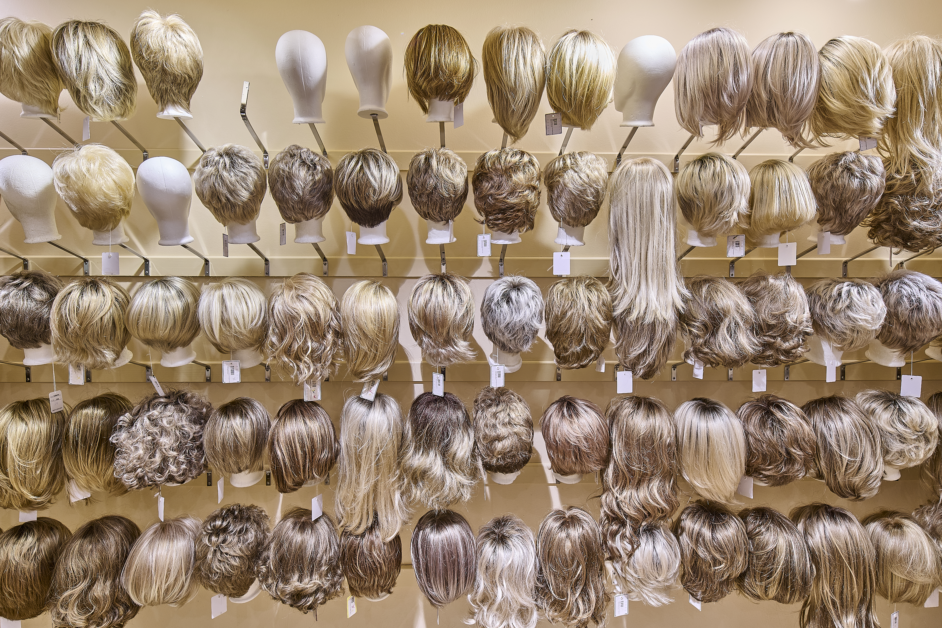 Eine Vielzahl unterschiedlicher Perücken hängt an einem Verkaufsregal.