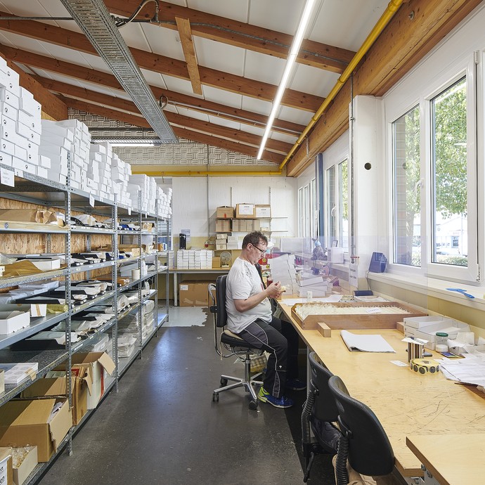 Ein Mann arbeitet sitzend in einem hellen langen Raum an einem Tisch. Hinter ihm befinden sich Lagerregale, vor ihm Fenster. (vergrößerte Bildansicht wird geöffnet)