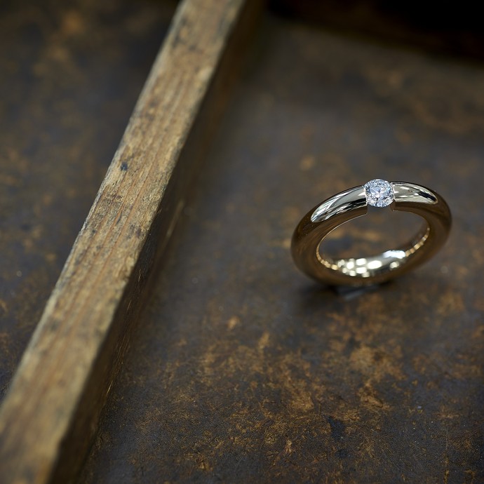 Ein Ring mit Diamant auf hölzernem Untergrund. (vergrößerte Bildansicht wird geöffnet)