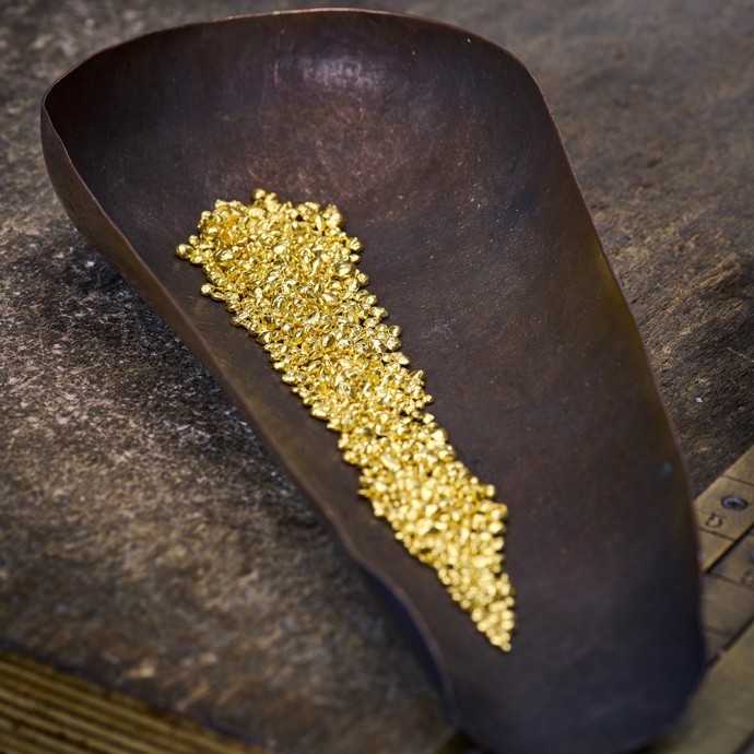 Kleine Goldnuggets liegen in einer braunen Schütte. (vergrößerte Bildansicht wird geöffnet)