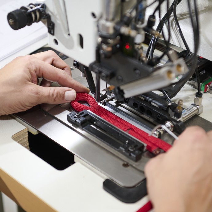 Die Hände eines Mannes richten ein Seil in einer Industrienähmaschine aus. (vergrößerte Bildansicht wird geöffnet)